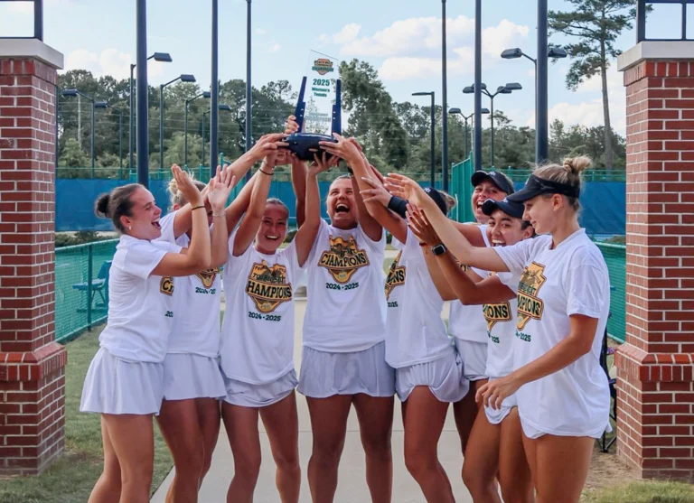 Linn Goerdes lifting the 2025 tennis conference championship trophy with her teammates.